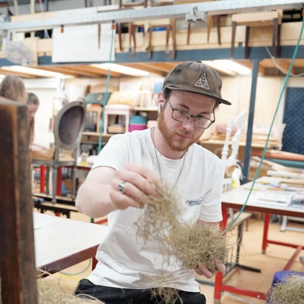 Een student van het Hout en Meubileringscollege stoffeert een stoel.