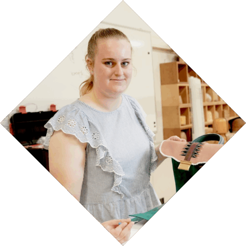 Student is bezig met het maken van een tas en kijkt trots de camera in