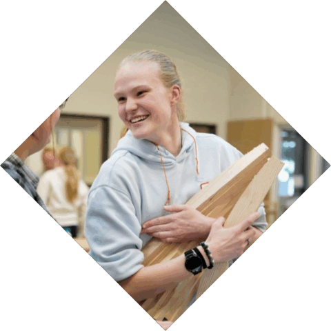 Student heeft hout in handen en lacht naar een andere student