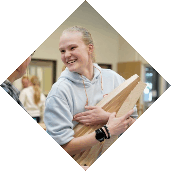 Student heeft hout in handen en lacht naar een andere student